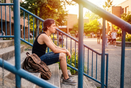 Thoughtful teenage boy sitting alone on school outdoor stairs with backpack, adolescent mental health and solitude concept