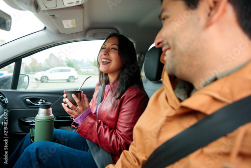 Joyful Latina woman holding yerba mate and laughing with friend inside car