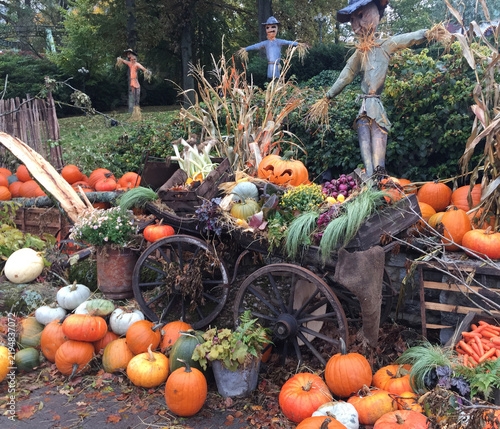 Rustic wooden cart filled with colorful pumpkins, gourds, and scarecrows in an autumn harvest display.
