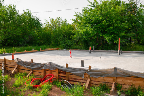 New concrete slab foundation under construction with exposed utility pipes and timber formwork at a residential building site, showing an early stage of house construction