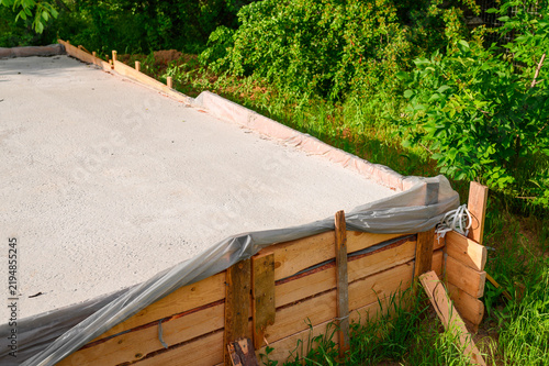Close view of a concrete slab foundation under construction with timber formwork and protective plastic, documenting structural groundwork for a new residential building project