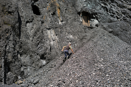 Miner climbing steep mountain slope towards mine entrance