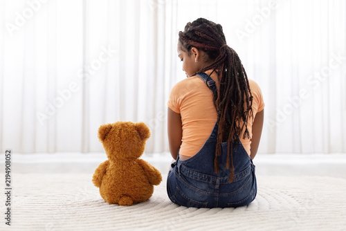 Canvastavla Black teenage girl sitting on the floor beside teddy bear at home, creating a qu