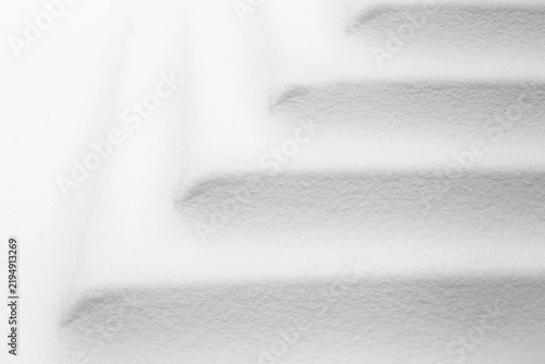 Vue rapprochée d'une portion d'escalier couverte de neige blanche. On devine la forme des marches ainsi que les coins grâce aux lignes et aux ombres grisâtres.   