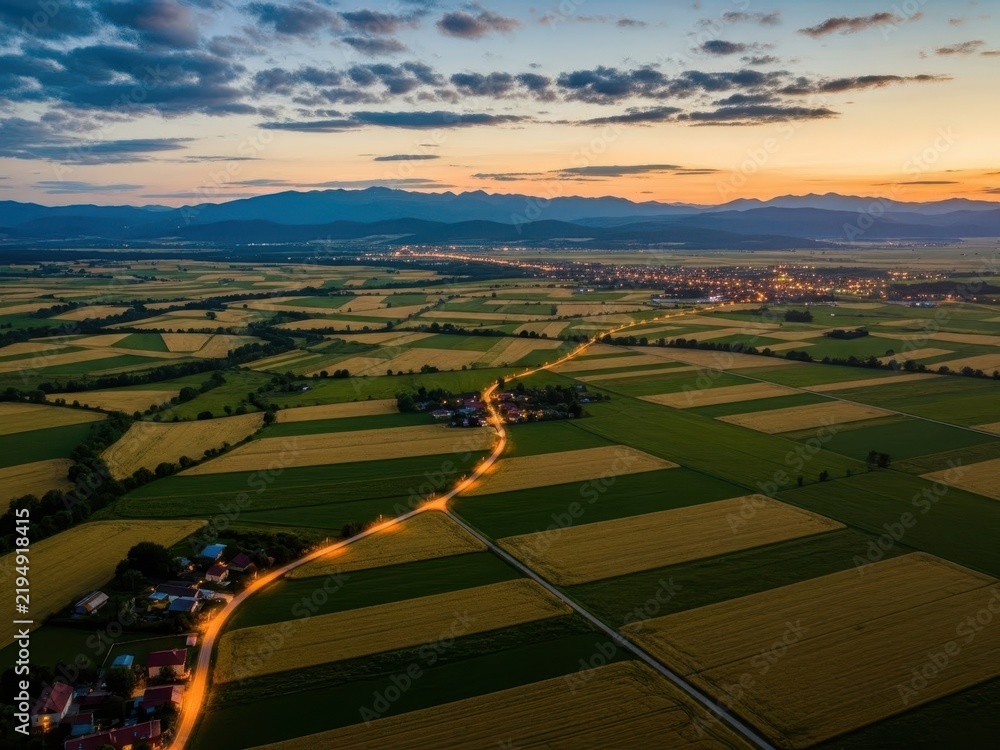 Obraz premium Aerial view of winding country road through green fields at sunset