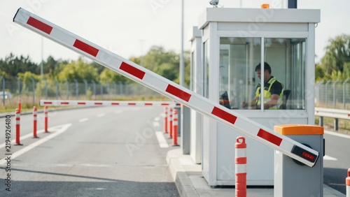 Security guard in a toll booth with a raised white and red barrier arm