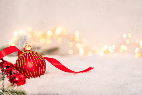 Red and gold Christmas baubles with ribbon resting on snow  surrounded by warm fairy lights in a cozy  festive holiday setting. Ideal for holiday greeting cards  festive banners.