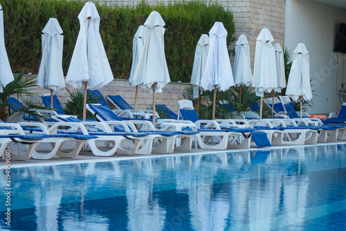 Obraz na płótnie Swimming pool area with sunbeds and closed umbrellas at resort