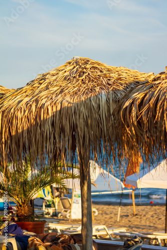 Quadro su tela Straw beach umbrella on a sandy sea beach in warm sunlight
