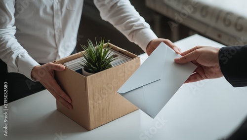 Close up of employee handing resignation letter to manager with cardboard box.
