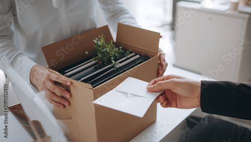 Close up of employee handing resignation letter to manager with cardboard box.
