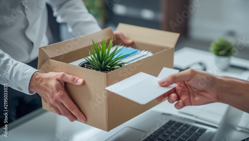 Close up of employee handing resignation letter to manager with cardboard box.

