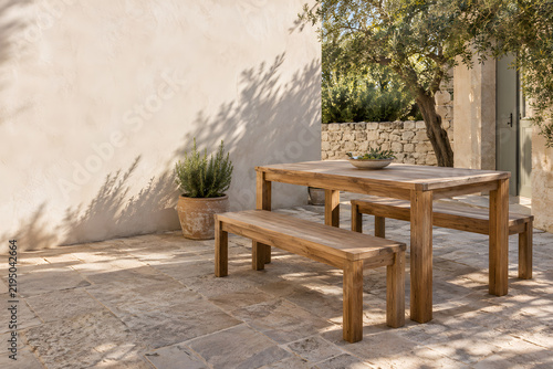 Mediterranean courtyard with wooden dining table and benches in warm sunlight