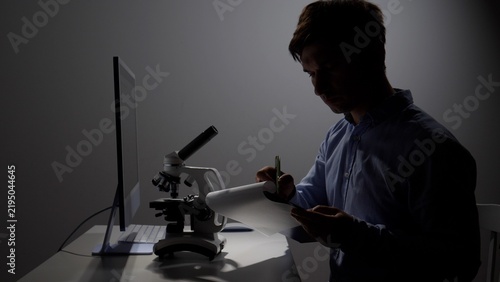 Foto Male scientist in a darkened lab workspace intently writing observations on a cl