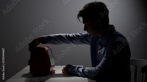 Fotografie Man reaching for a retro television, casting a strong silhouette in a dimly lit