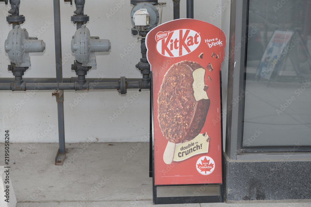 Obraz premium gas pipes and sidewalk a-frame poster sign of Kit Kat Double Crunch outside Friends Corner Convenience Store, 34 Freeland St (The Prestige), Toronto