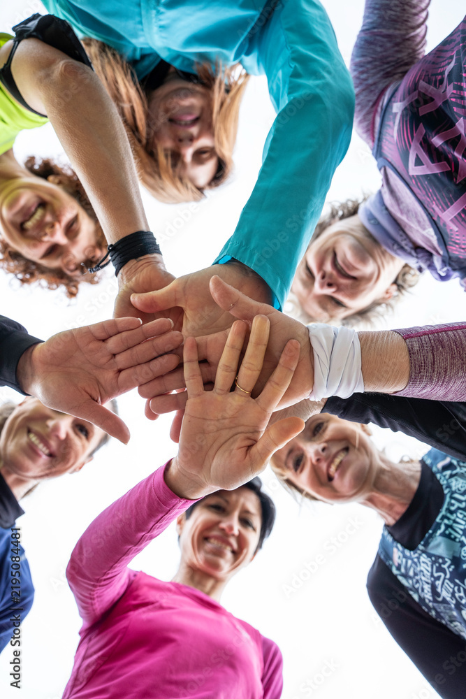 Fototapeta premium Generation x and baby boomer women stack hands in a low-angle fitness huddle. Energetic outdoor group expresses teamwork, unity, motivation, active aging, and female solidarity.