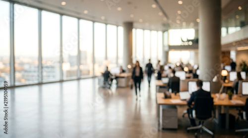 Blurred corporate office interior featuring busy professionals working at desks during bright sunny day time
