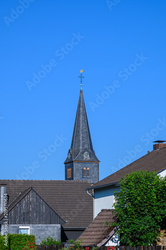 Bild auf Leinwand Traditional church steeple rising above residential rooftops under a blue sky