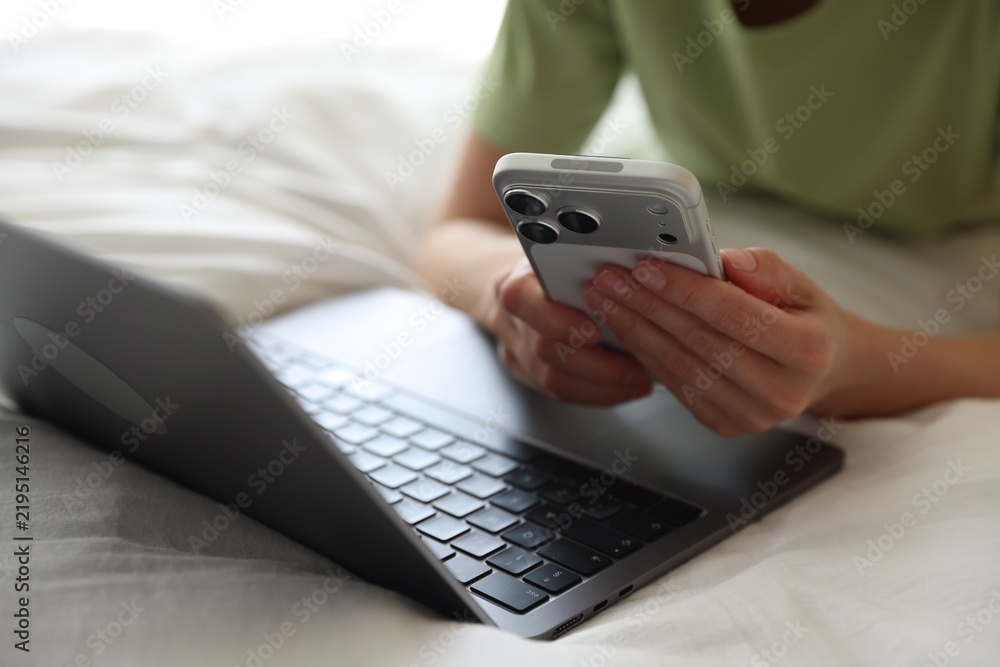 Obraz premium Woman with laptop and smartphone in bed at home, closeup
