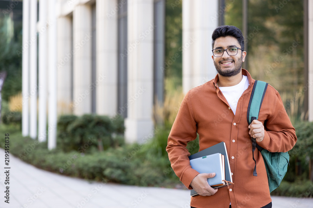 Obraz premium Happy Indian student with backpack and books, university education and academic success.
