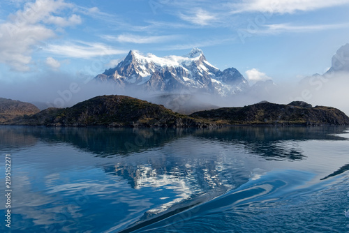 Snow covered peaks of Torres del Paine rising above morning fog and turquoise glacial waters of Lake Pehoe in Chilean Patagonia.