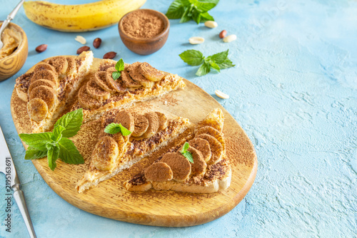 Toast bread with peanut butter and fried banana on a textured blue stone surface. Tasty dessert ready to eat. Copy space.