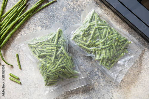 Fresh green beans, vacuum-sealed, in a packaging and vacuum sealer on a light gray background. Healthy eating, zero waste, and meal prep concept. Top view, flat lay. Copy space.