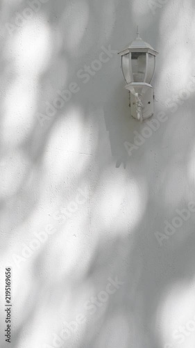 Vintage Wall Lantern with Moving Tree Shadows on White Stucco Wall, Sunlight and Architectural Background.