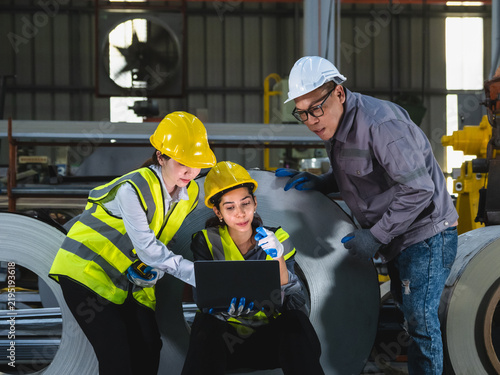 Diverse Industrial Engineer Collaborating with Laptop in Steel Factory: Multiethnic team hardhat discussing technical data and coil inventory ideal smart manufacturing teamwork concept.