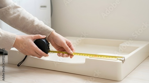 Woman using tape measure to measure washing machine drain pan tray on laundry floor