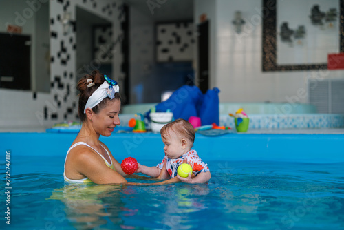 Fotografía A woman in a swimsuit holds an infant holding a ball in an indoor swimming pool