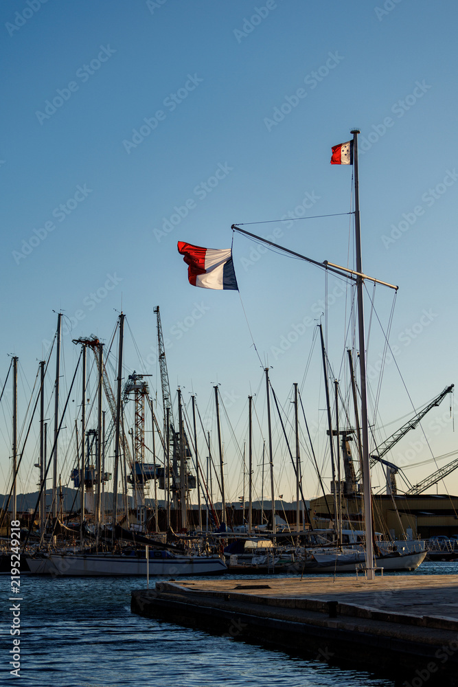 Fototapeta premium Large French national flag waving on a mast at a harbor shipyard