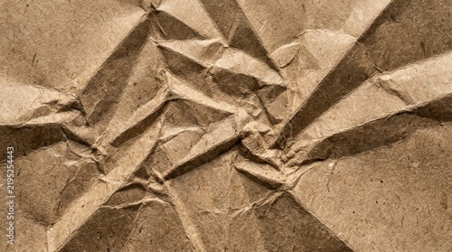 Crinkled brown kraft paper texture displays a heavily folded and rumpled surface crumpled creased wrinkled rippled textured cardboard material background abstract close up detail rough uneven
