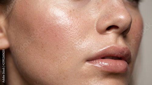 Extreme macro beauty portrait of a woman highlighting dewy skin texture, natural pores, subtle freckles, and a glossy cheekbone with clean lighting.