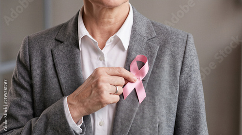 Businesswoman wearing pink ribbon on blazer to show breast cancer awareness and support in corporate environment.