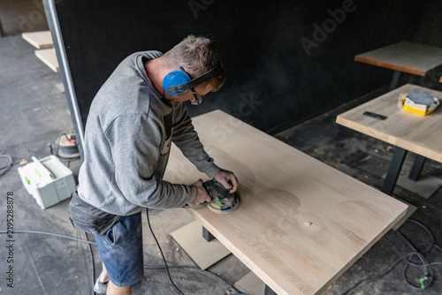 Craftsman Sanding Large Wooden Table in Furniture Workshop