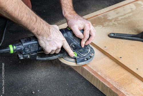 Close Up of Craftsman Sanding Wooden Table Edge with Power Sander