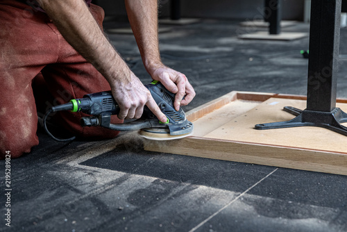 Craftsman Sanding Edge of Upside Down Wooden Table During Restoration