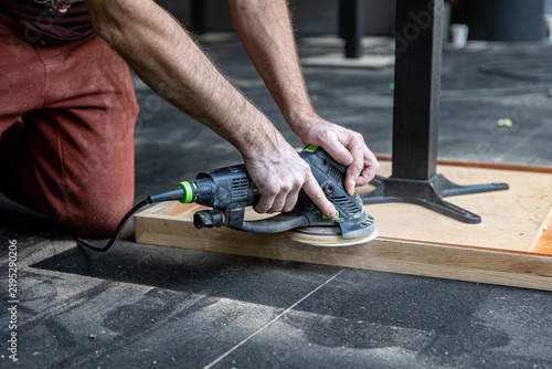 Craftsman Sanding Edge of Upside Down Wooden Table During Restoration