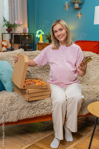 Fotografie Pregnant middle-aged woman at home ordering pays pizza order on smartphone banking app satisfied waiting for meal
