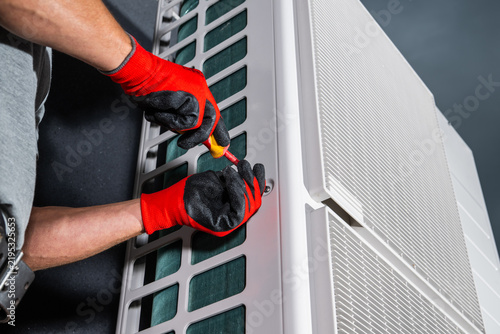 Technician using a screwdriver on an outdoor HVAC unit