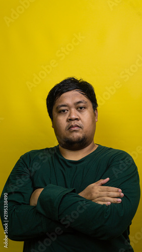 фотографія Young Asian male stands with crossed arms against vibrant yellow background, projecting serious and confident demeanor