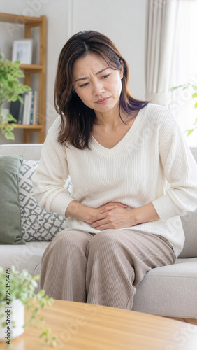 室内で下腹部の痛みや更年期の不調に悩みお腹を押さえる女性