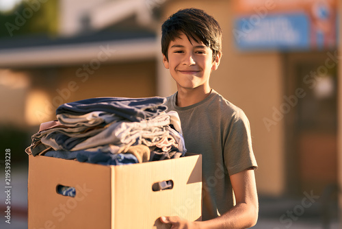 A Hispanic teenager is transporting a box of donated clothes for a charity initiative