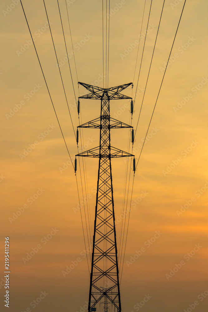 Obraz premium Symmetrical high-voltage electricity transmission tower silhouette against a golden sunset sky