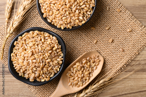 Whole wheat grain in a black bowl and wooden scoop, Food ingredients, Table top view