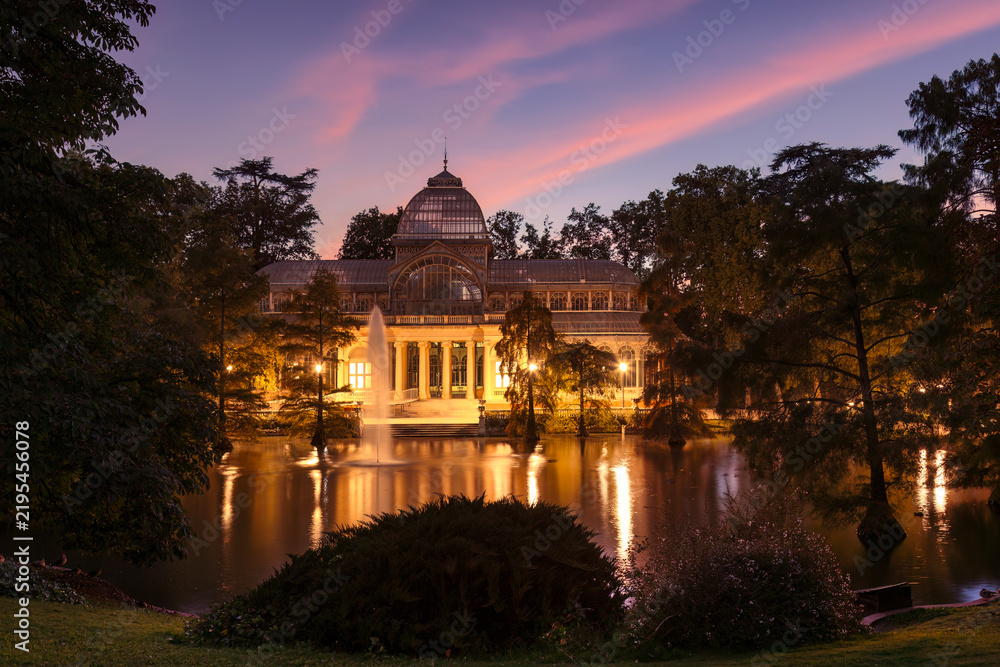 Obraz premium Magical sunset at Palacio de Cristal (Glass Palace) in El Retiro Park, Madrid, with colorful clouds reflecting in the lake