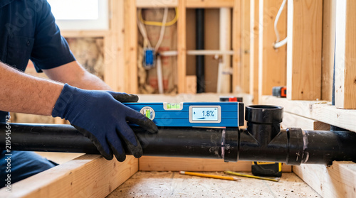 Plumber Using Digital Level to Accurately Check Slope of Drainage Pipe on Construction Site
