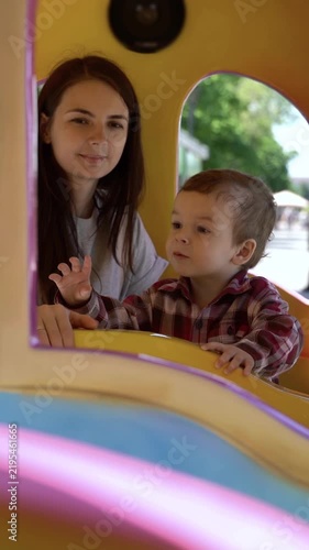 Mother and little son riding in a colorful children's train at an amusement park on a sunny day.